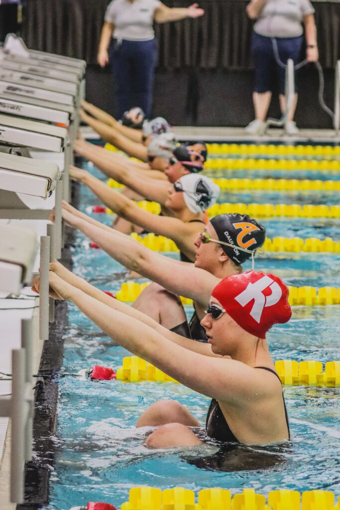 Women swimmers at starting blocks during a race in an indoor swimming pool, focused on competition.